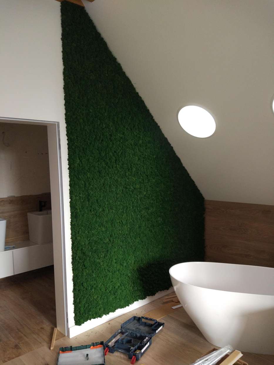 Montaż dużej ściany z mchu chrobotka w łazience na poddaszu z wolnostojącą wanną, okrągłym oświetleniem i widocznymi narzędziami montażowymi.