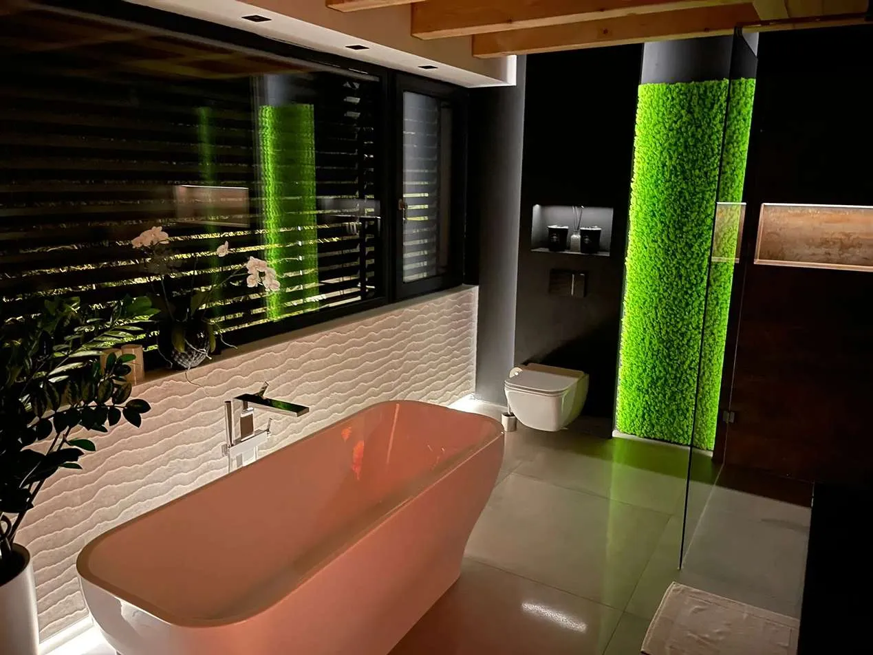 Nowoczesna aranżacja łazienki ze stojącą wanną, żaluzjami i pionowym panelem z mchu chrobotka w intensywnym, jasnozielonym kolorze na czarnymi tle.